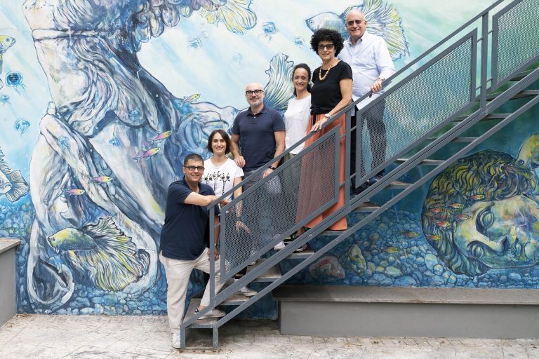 gruppo di persone su una scala che sale lateralmente con sfondo muro con grafiti colorati tonalità azzurro